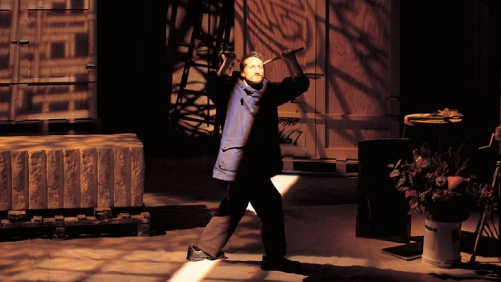 attore su palco con braccia alzate alla nuca sostiene due oggetti, guarda verso l'alto